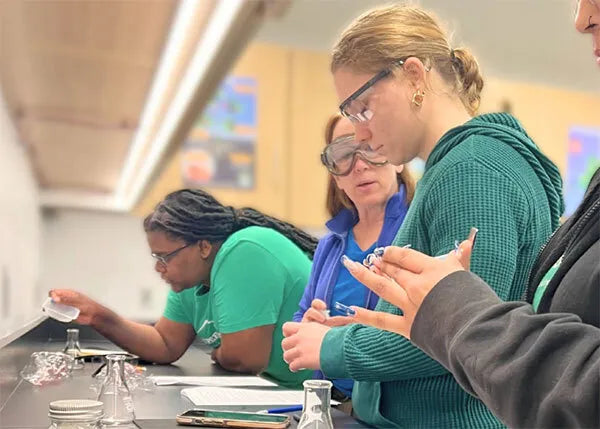 Interns at No More Empty Pots conducting a hands-on science experiment in a lab setting, wearing goggles and collaborating with focus and curiosity.
