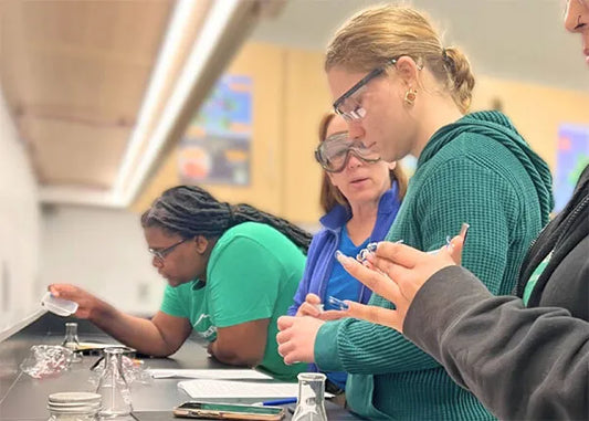 Interns at No More Empty Pots conducting a hands-on science experiment in a lab setting, wearing goggles and collaborating with focus and curiosity.